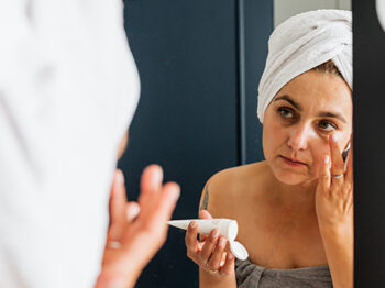 woman putting on moisturizer looking into mirror