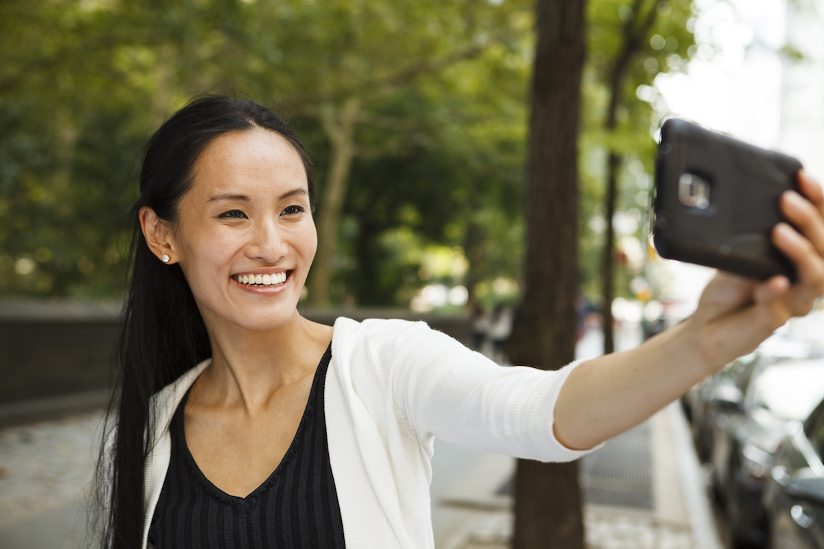 A young happy woman taking a selfie with her smartphone. For beginner's guide to your first filler treatment Dr. Irwin answers on Skintour