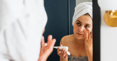 woman putting on moisturizer looking into mirror