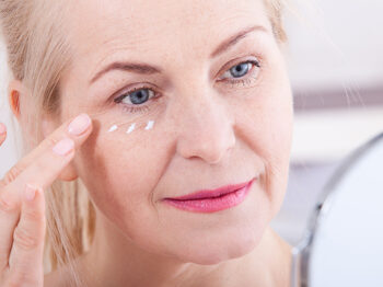 woman applying eye cream in mirror